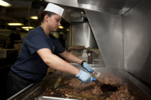 female cook grilling steak on a large stove top