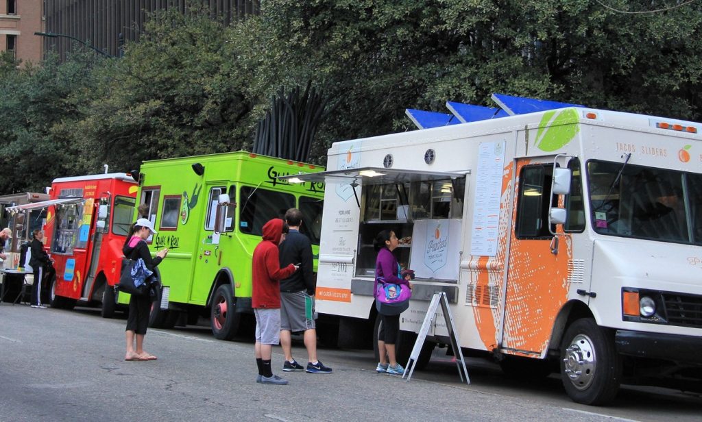 three people waiting in line for food in front of a food truck